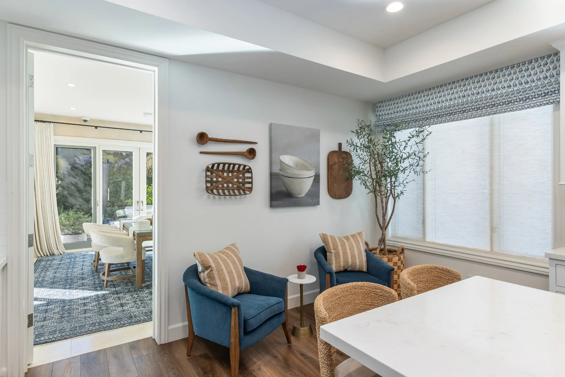 Breakfast nook in a custom Brentwood home featuring woven chairs, blue accent armchairs, wall-mounted art, and natural light from a large window.