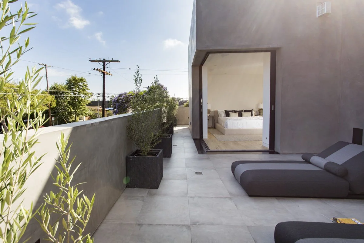Indoor-outdoor bedroom suite with floor-to-ceiling sliding glass door opening to private Venice terrace with planters and lounge seating.