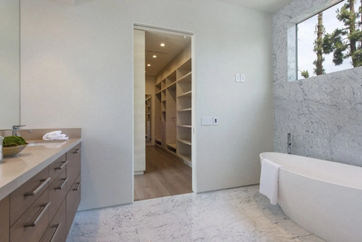 Primary bathroom in West Hollywood custom home with marble tub surround and walk-in closet beyond.