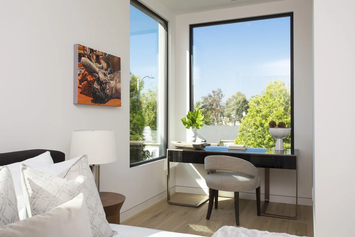 Compact home office nook with floating desk framed by corner windows, natural daylight, and treetop views.