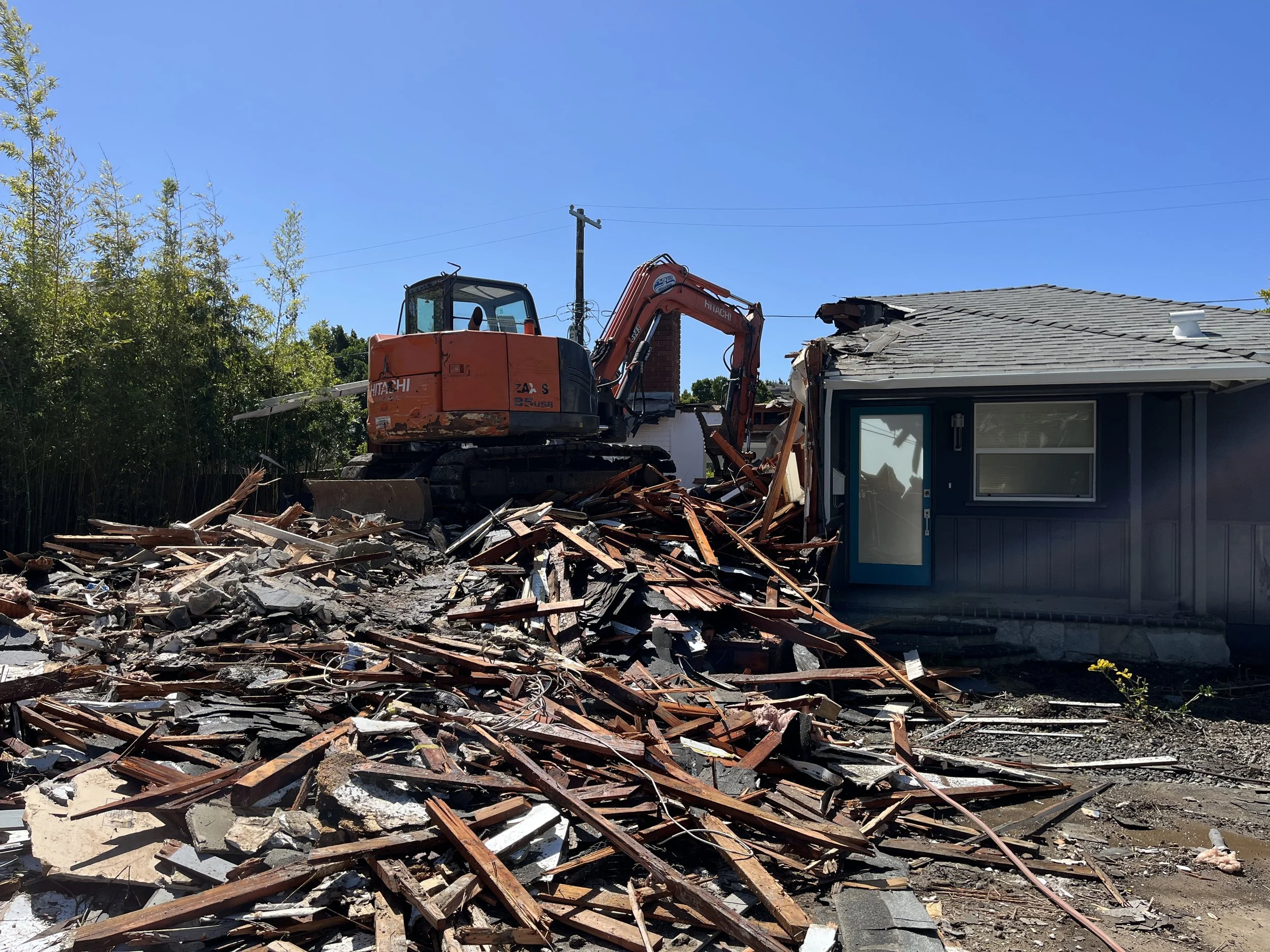 Active teardown of single-story house with excavator and debris during site demolition phase