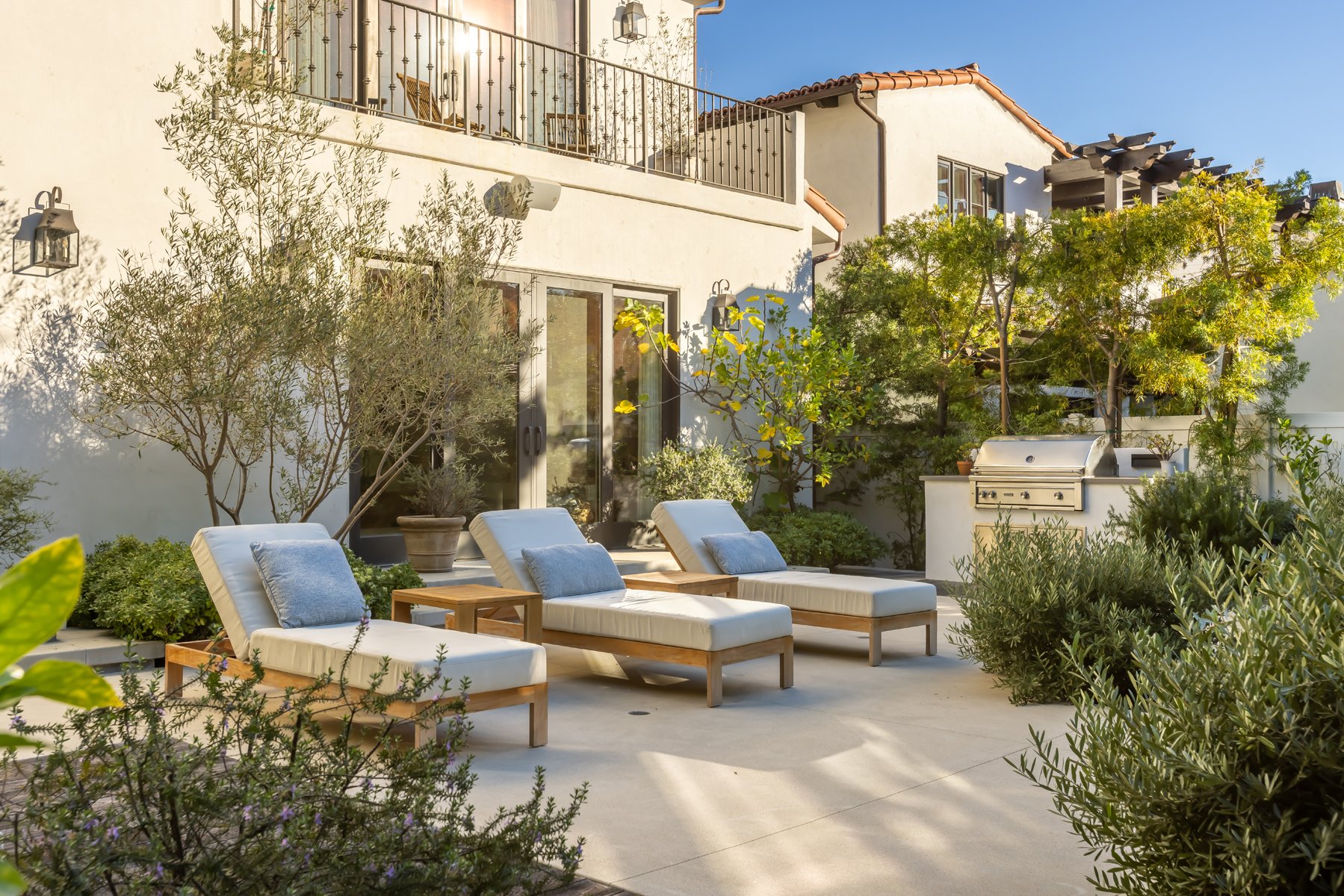 Outdoor patio of a custom Brentwood home with built-in grill, wood lounge chairs, and lush Mediterranean landscaping.