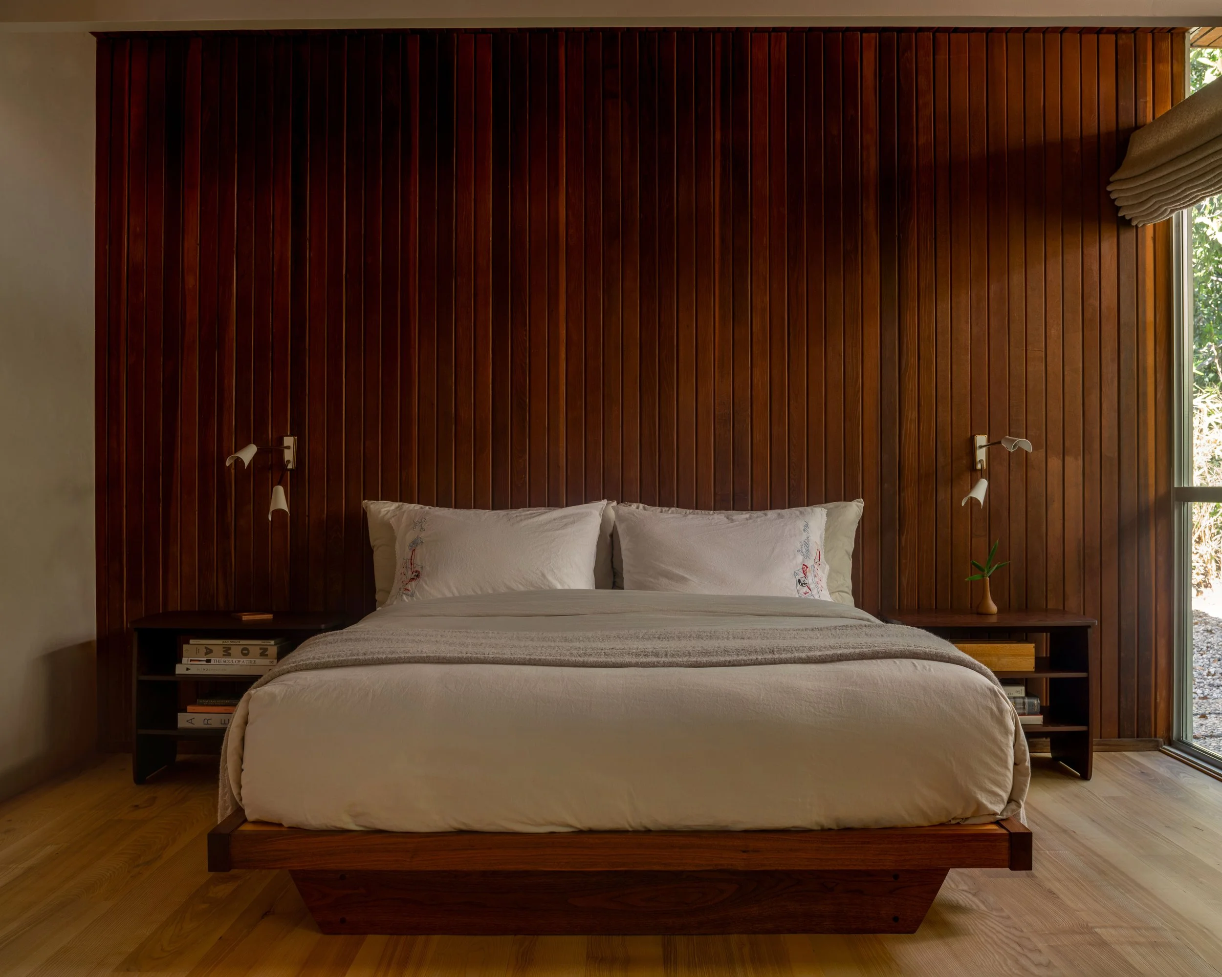 Custom walnut platform bed with vertical wood slat accent wall and built-in nightstands in the La Cuesta primary bedroom.