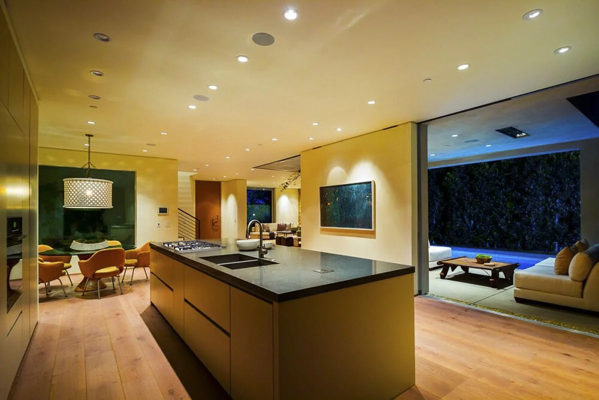 Open kitchen and dining area at night with sliding glass walls in West Hollywood custom home.