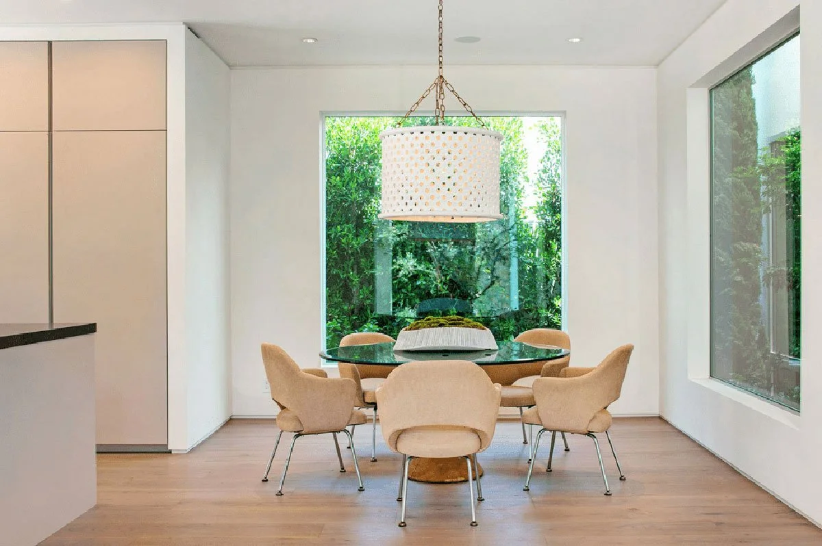 Dining area in West Hollywood modern home with round glass table and garden-facing window.