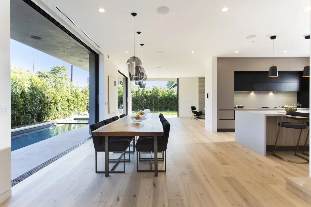 Venice indoor-outdoor living space with flush track sliding doors, oak floors, manicured lawn, and perimeter privacy hedging