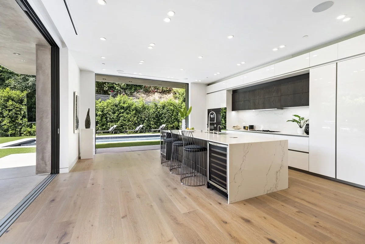 Beverly Hills modern kitchen with waterfall island, wide-plank oak floors, and full-height sliding glass doors opening to backyard