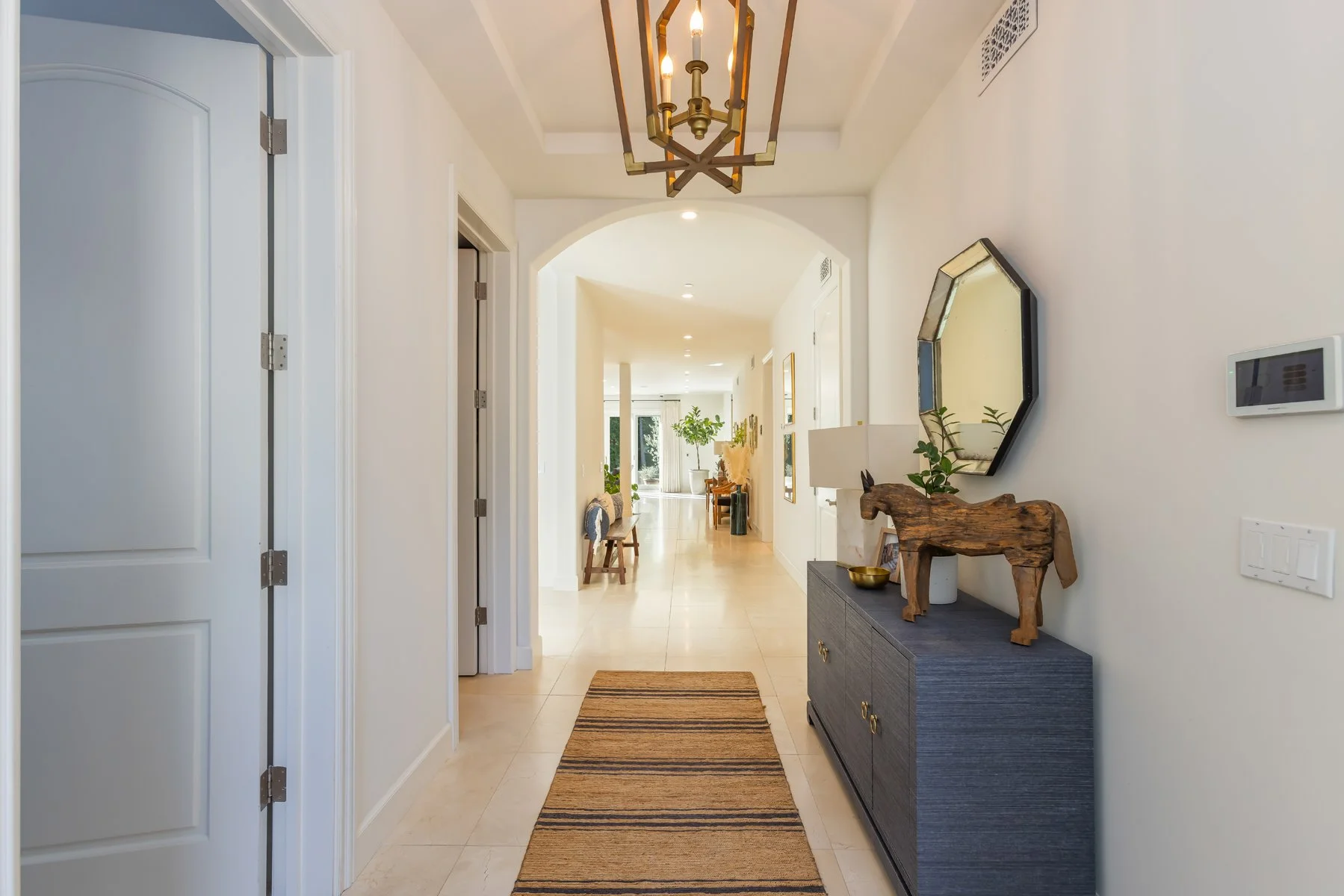 Interior hallway of a custom home in Brentwood, Los Angeles, featuring arched doorways, light stone flooring, a brass pendant light, and a styled console with decorative accents.