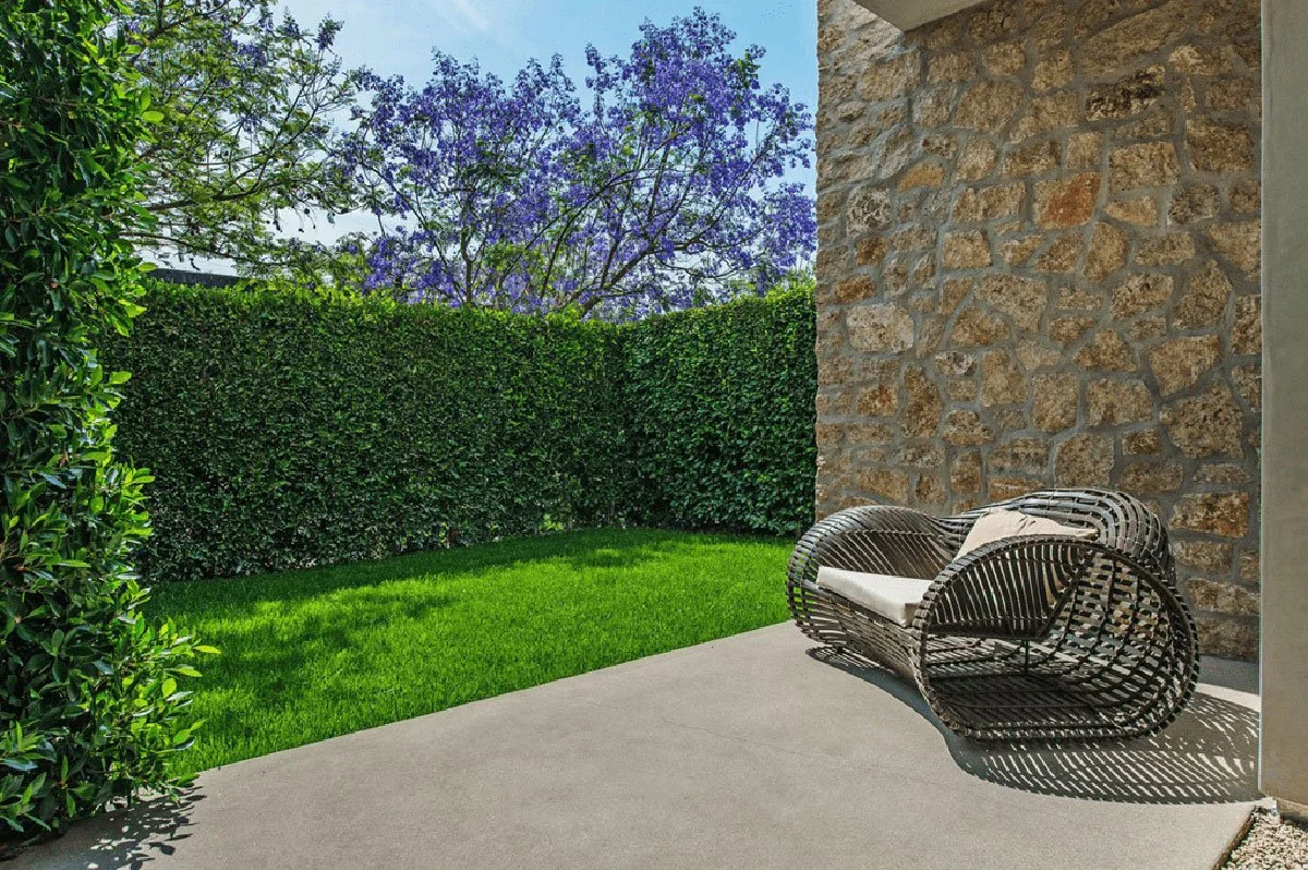 Landscaped garden corner with stone exterior wall and seating area at West Hollywood modern residence.