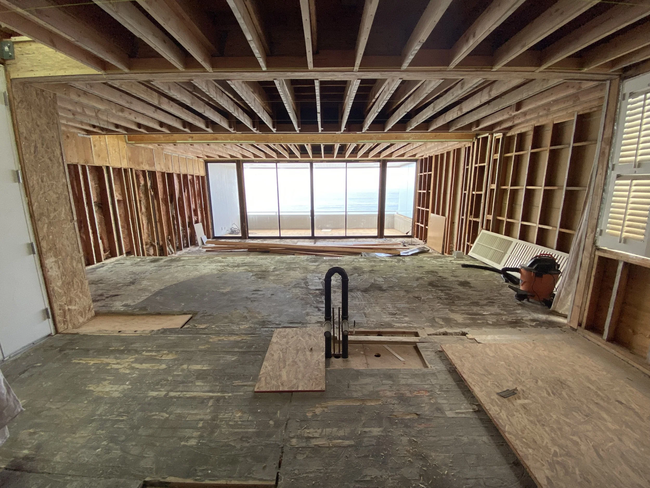 Malibu condo full gut renovation showing exposed framing and open structure aligned with ocean view through sliding glass doors