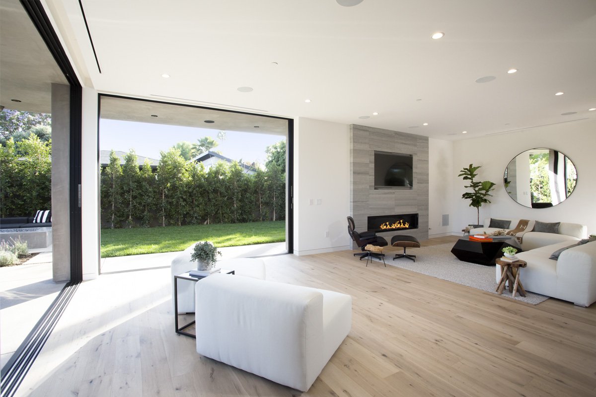 Venice indoor-outdoor living space with flush track sliding glass wall, linear fireplace, and manicured backyard lawn