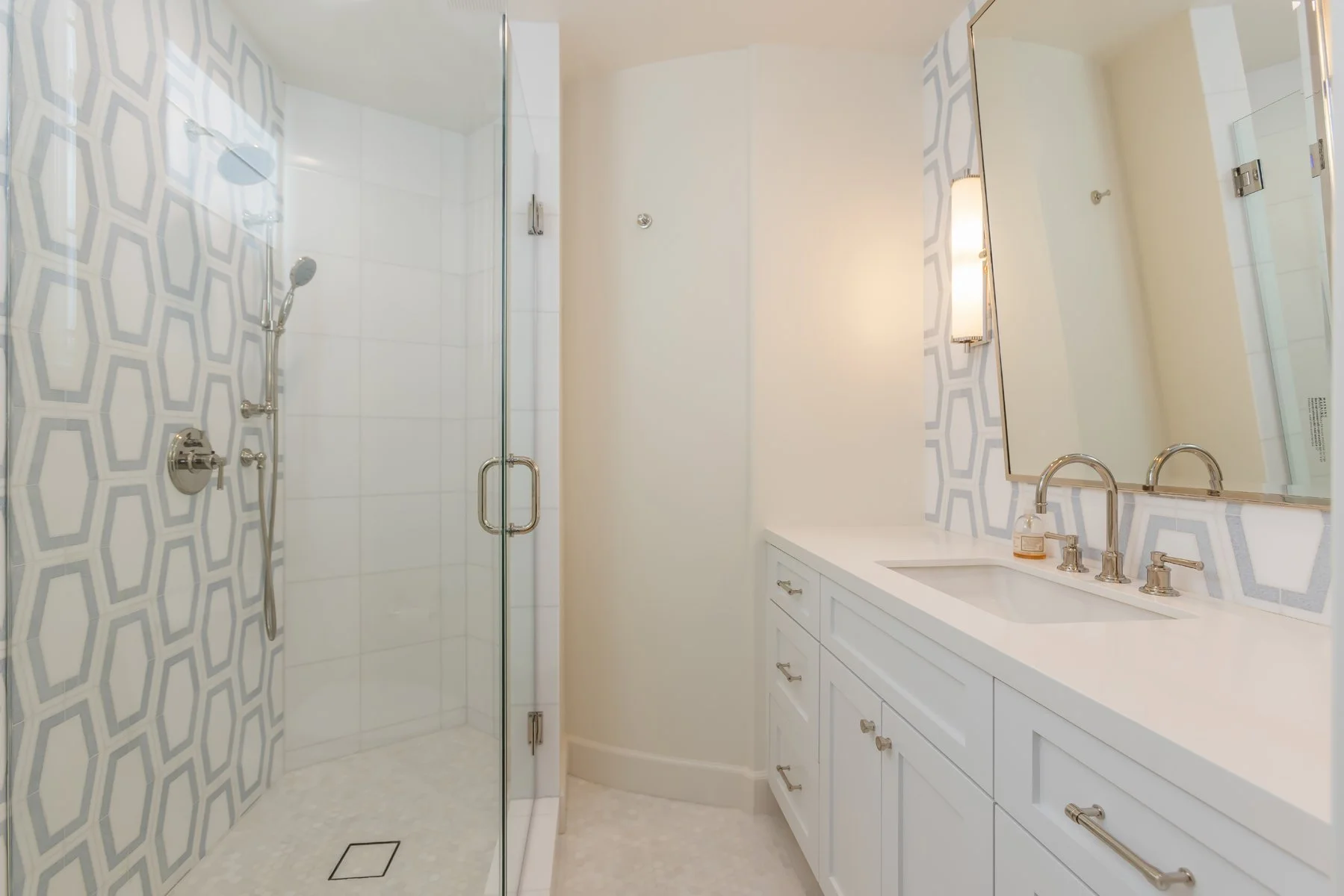 Guest bathroom in a custom Brentwood home featuring a glass-enclosed shower with patterned tile walls, white shaker vanity, integrated sink, and polished chrome fixtures.