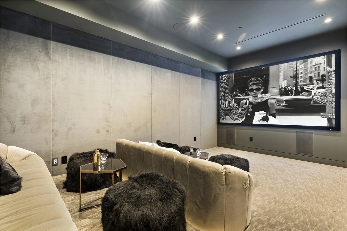 Beverly Hills home theater with oversized projection screen, concrete accent walls, and sculptural velvet seating