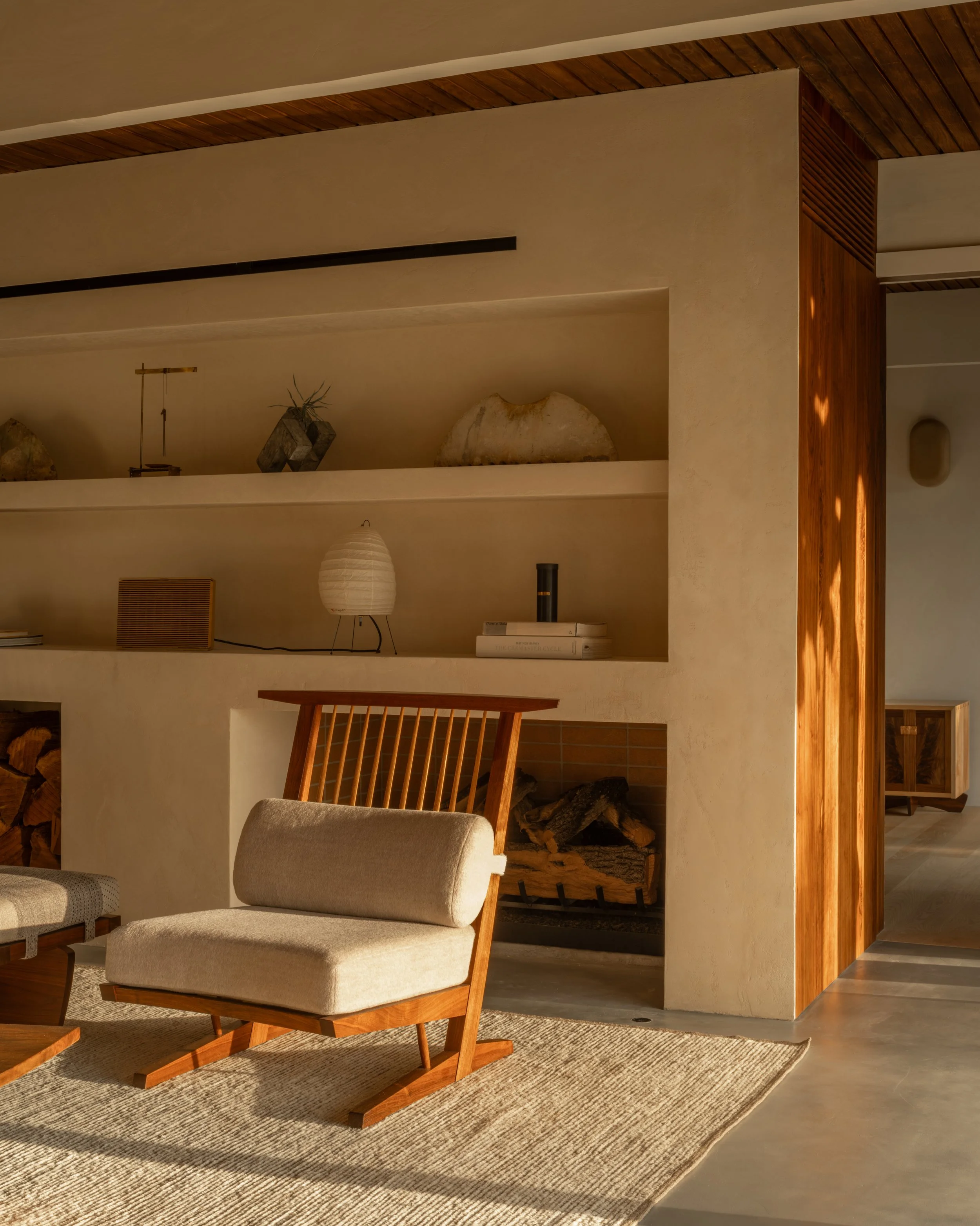 La Cuesta living room with custom plaster fireplace, built-in niche shelving, and walnut lounge chair in warm natural light.