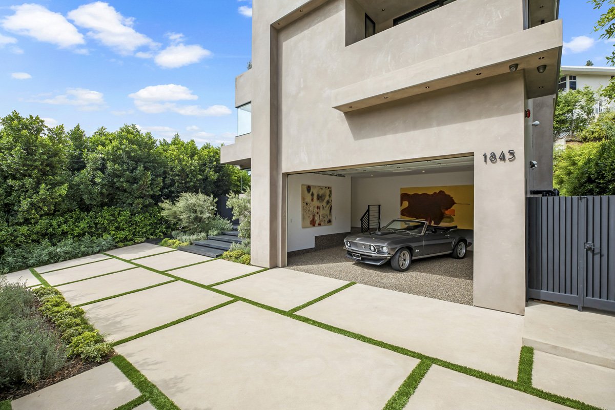 Modern Brentwood custom home with clean stucco façade, architectural driveway, and open garage design by Heart Construction.