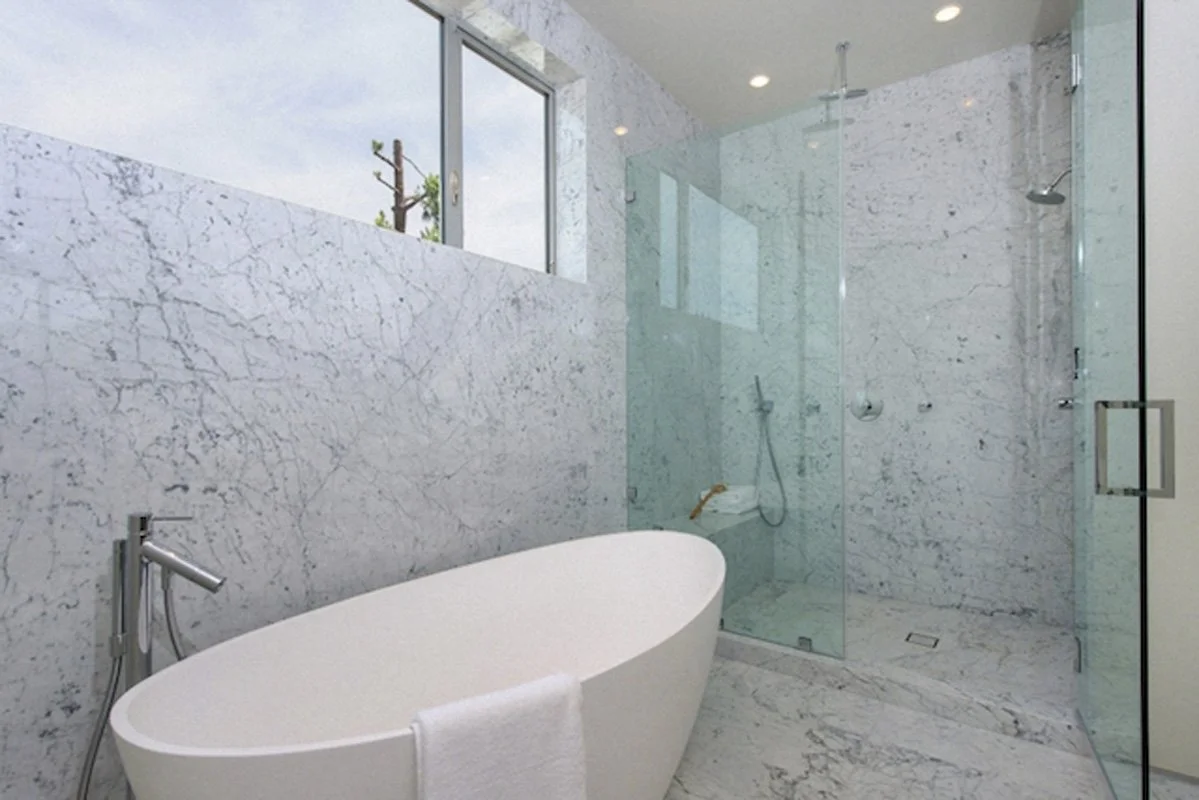Modern bathroom in West Hollywood residence with freestanding tub, marble walls, and glass shower.