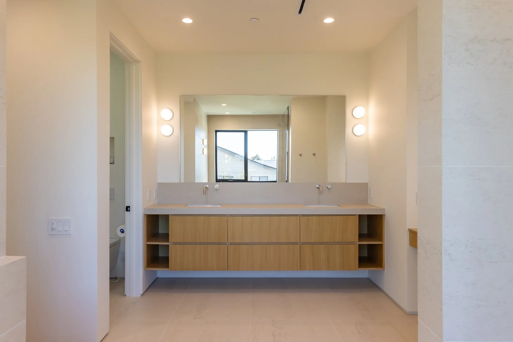 Modern Mar Vista primary bathroom with floating double vanity in light wood, integrated stone countertop, wall-mounted faucets, oversized mirror with minimal sconces, and clean contemporary design.