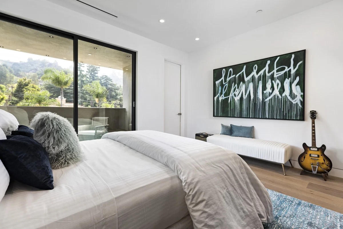 Beverly Hills guest bedroom with upholstered platform bed, wide-plank oak flooring, and sliding glass doors to terrace