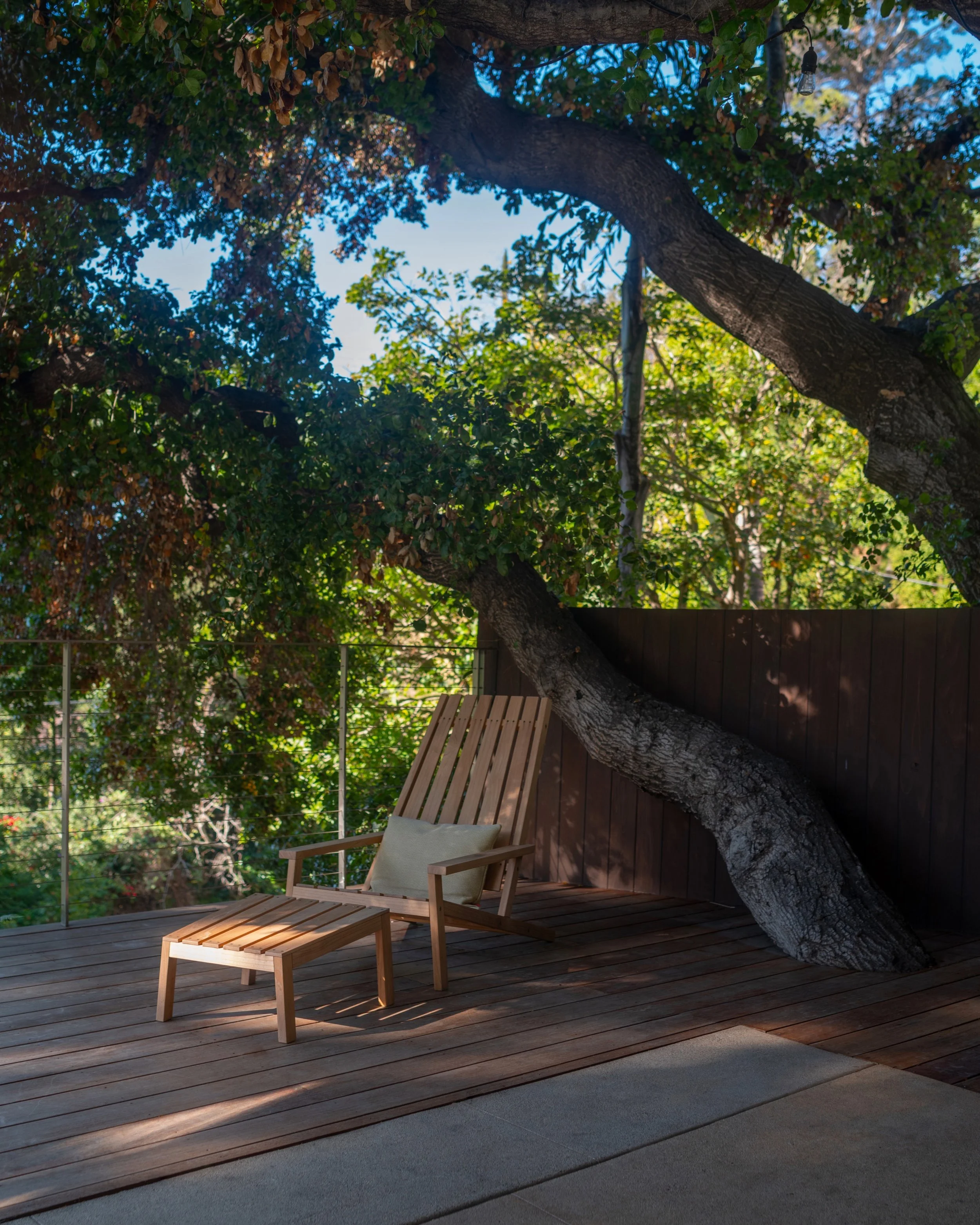 La Cuesta outdoor deck with custom wood lounge chair beneath mature oak tree and warm natural hillside setting.