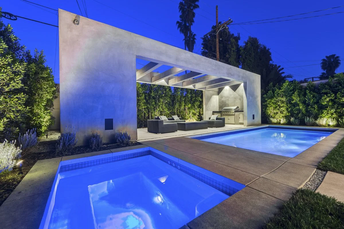 West Hollywood custom home backyard with pool, spa, and concrete outdoor pavilion with fire feature at night