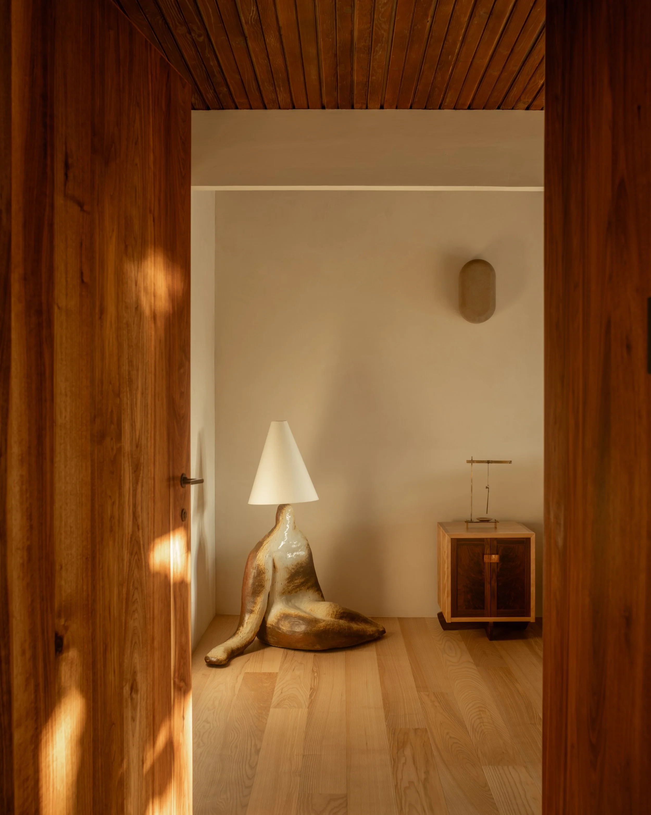 La Cuesta interior vignette with custom walnut doors, sculptural ceramic floor lamp, and minimalist wood nightstand in warm natural light.