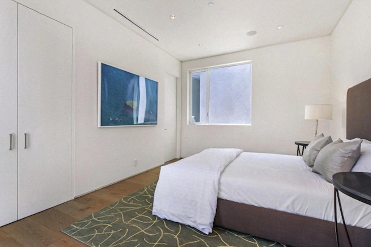 Bright bedroom in West Hollywood modern home with wood floors, white walls, and city-facing window.