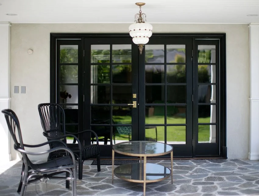 Covered patio with black French doors, stone flooring, and outdoor seating in Hancock Park backyard
