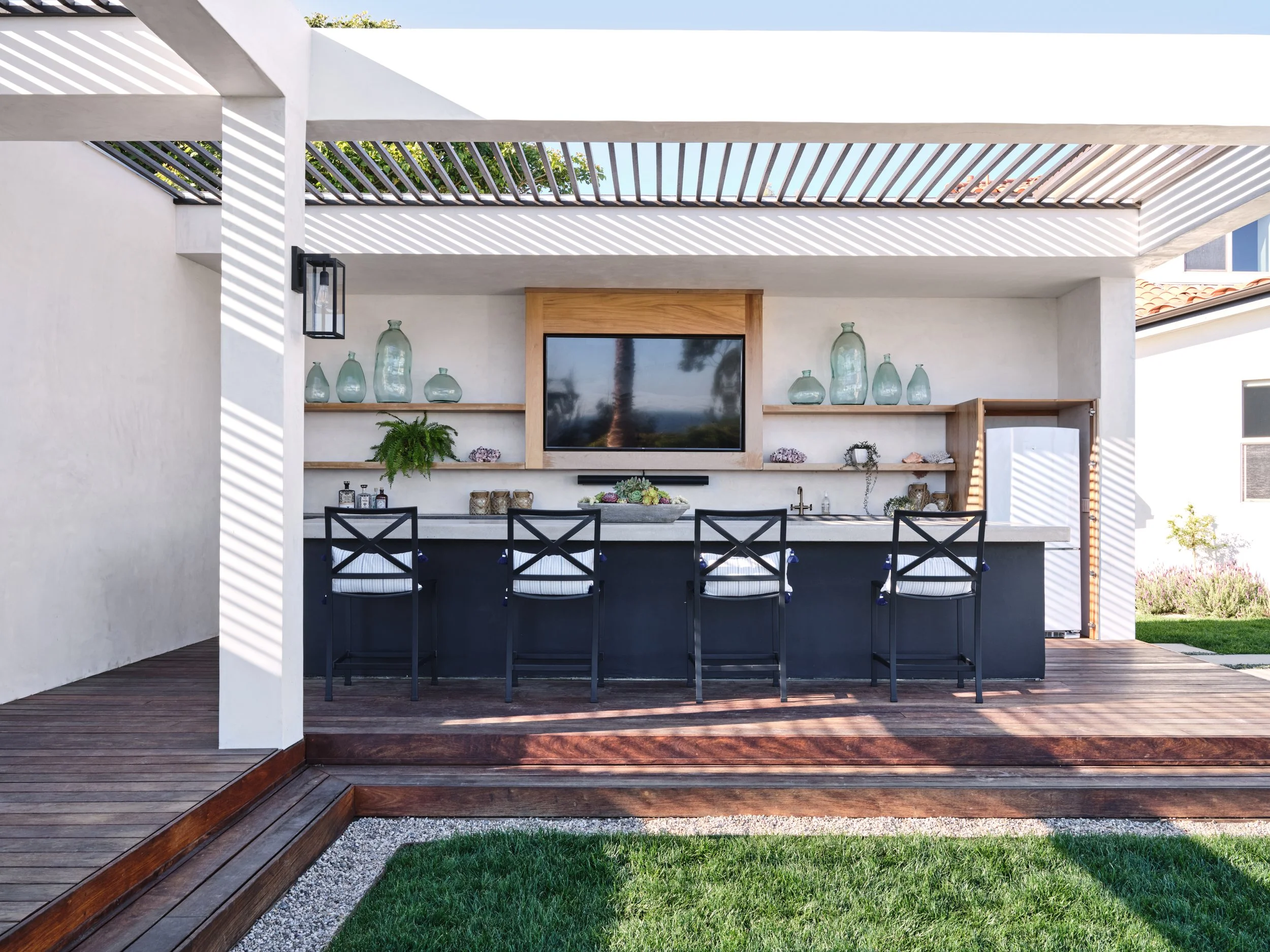 Malibu custom home outdoor bar with pergola, built-in seating, integrated TV, and outdoor kitchen designed and built by Heart Construction