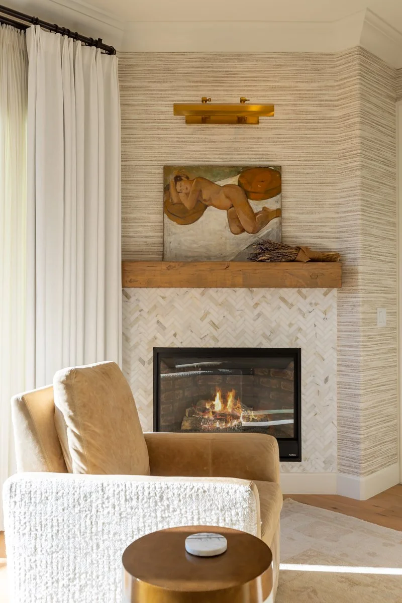 Fireplace detail in a Brentwood primary bedroom featuring a herringbone tile surround, wood mantel, framed artwork, textured wall covering, and warm brass accent lighting.