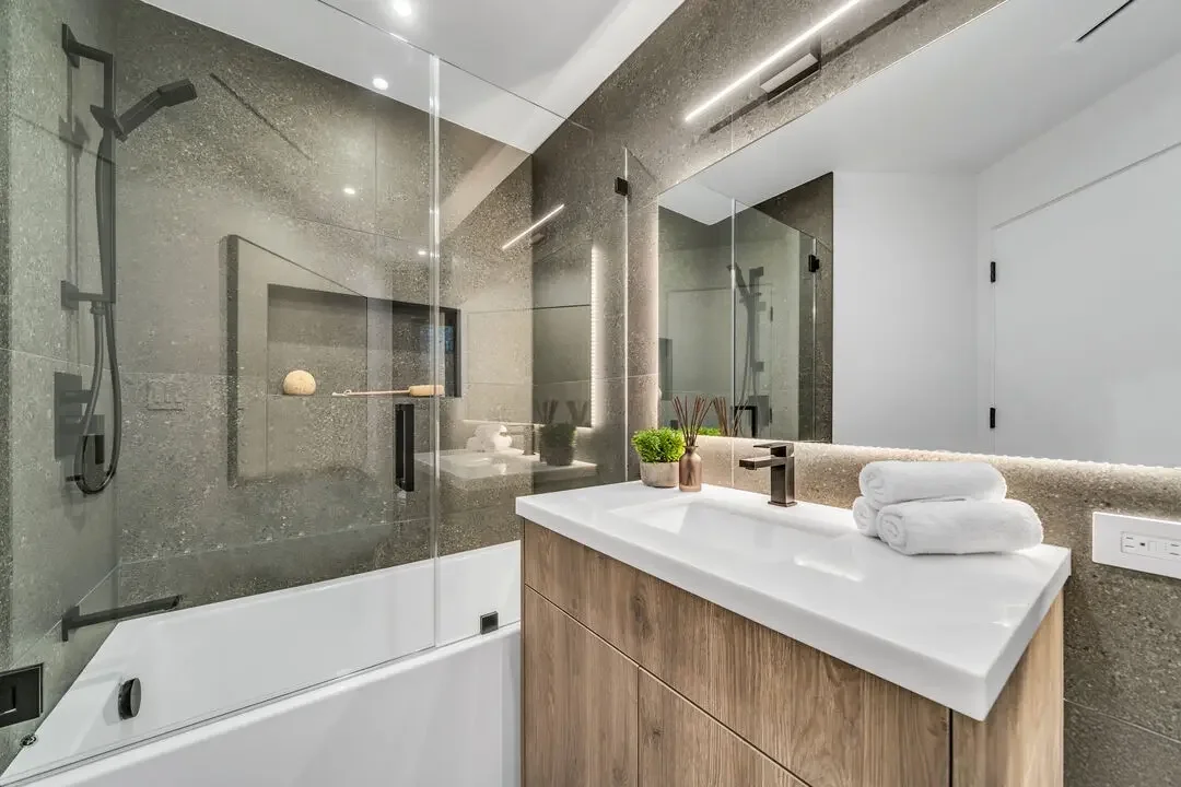 Modern bathroom with a bathtub, glass shower enclosure, vanity with a white sink, and decor including towels, plants, and reed diffusers.