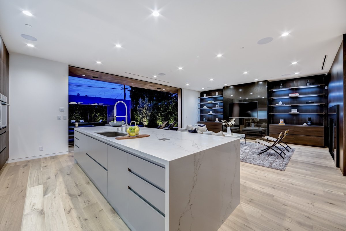 West Hollywood custom home kitchen with oversized quartz island and open living room overlooking illuminated backyard