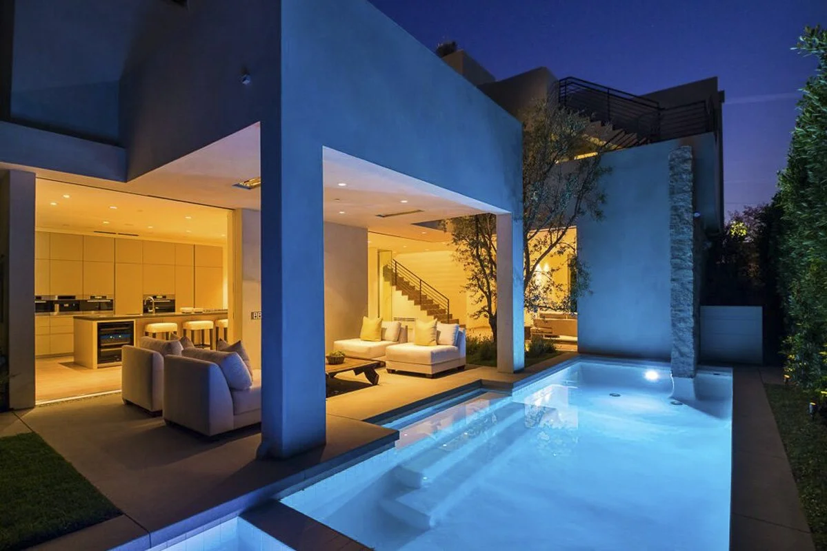Evening indoor–outdoor living space with pool and covered patio in West Hollywood custom home.