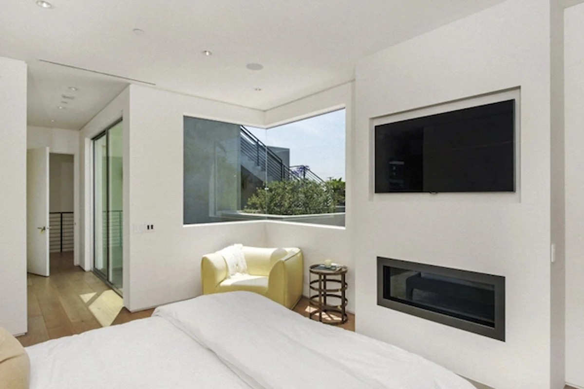 Modern bedroom in West Hollywood residence with corner window and contemporary fireplace.