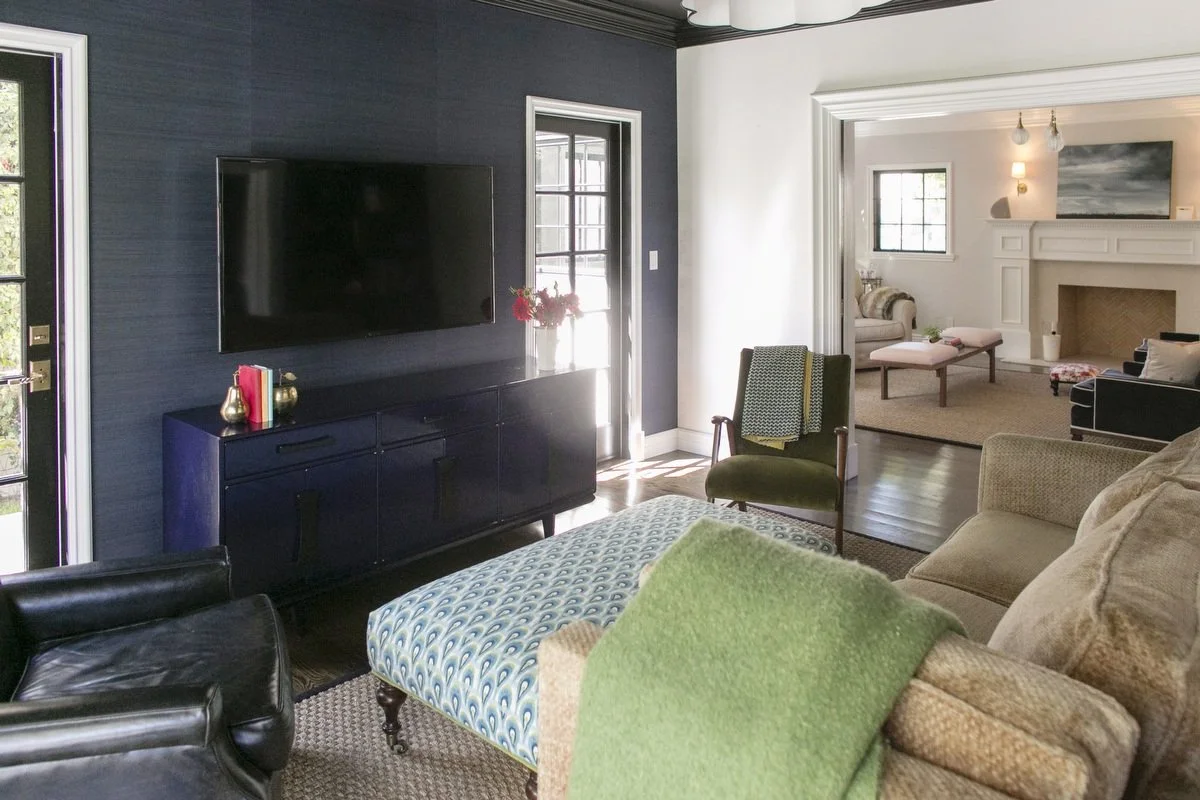 Moody family room with navy walls, media console, patterned ottoman, and view into formal living room
