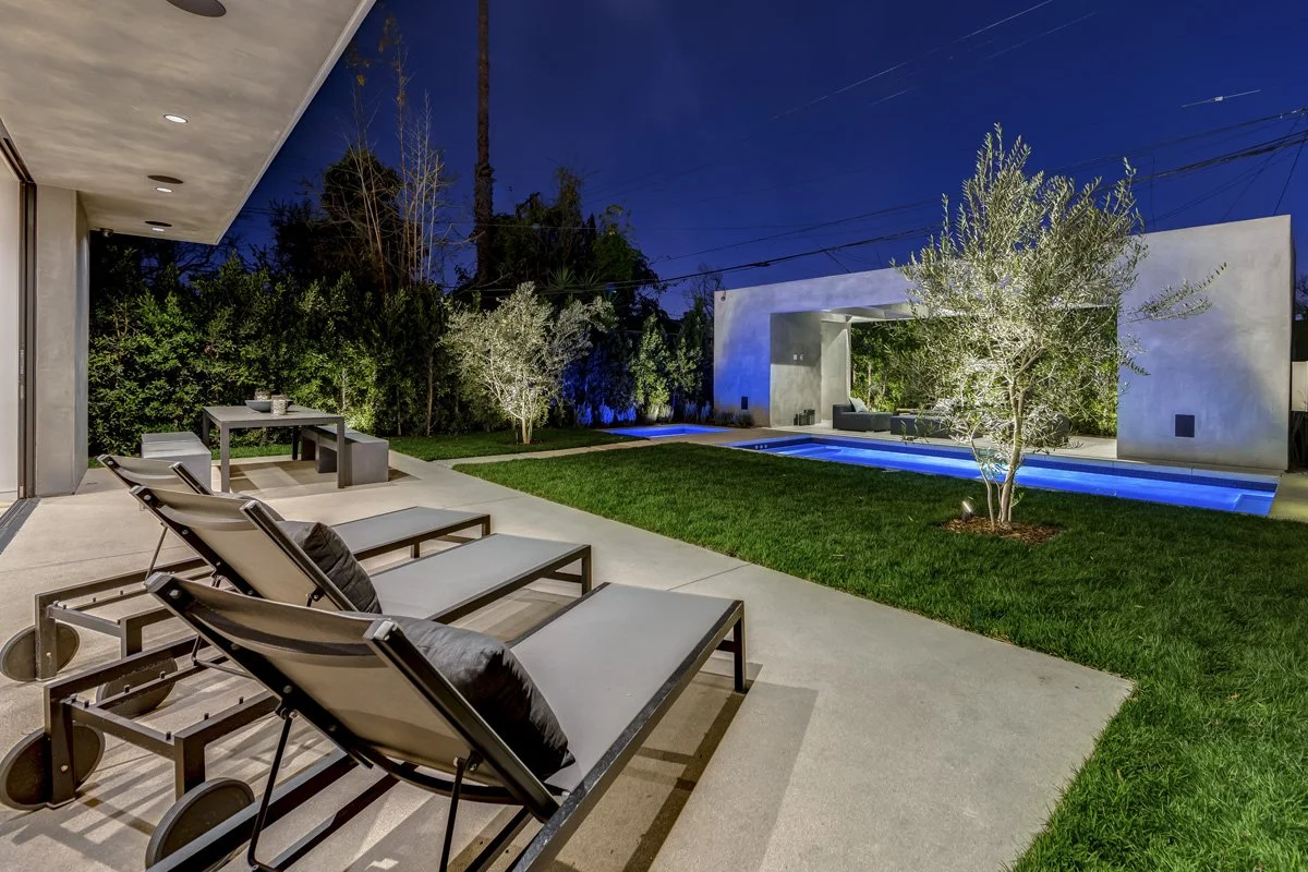 West Hollywood custom home backyard with pool, lawn, lounge chairs, and illuminated outdoor pavilion at night