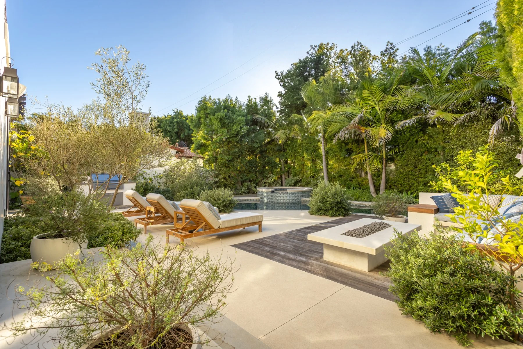 Landscaped backyard of a custom Brentwood home with lounge chairs, integrated fire pit, spa pool, and mature trees for privacy.