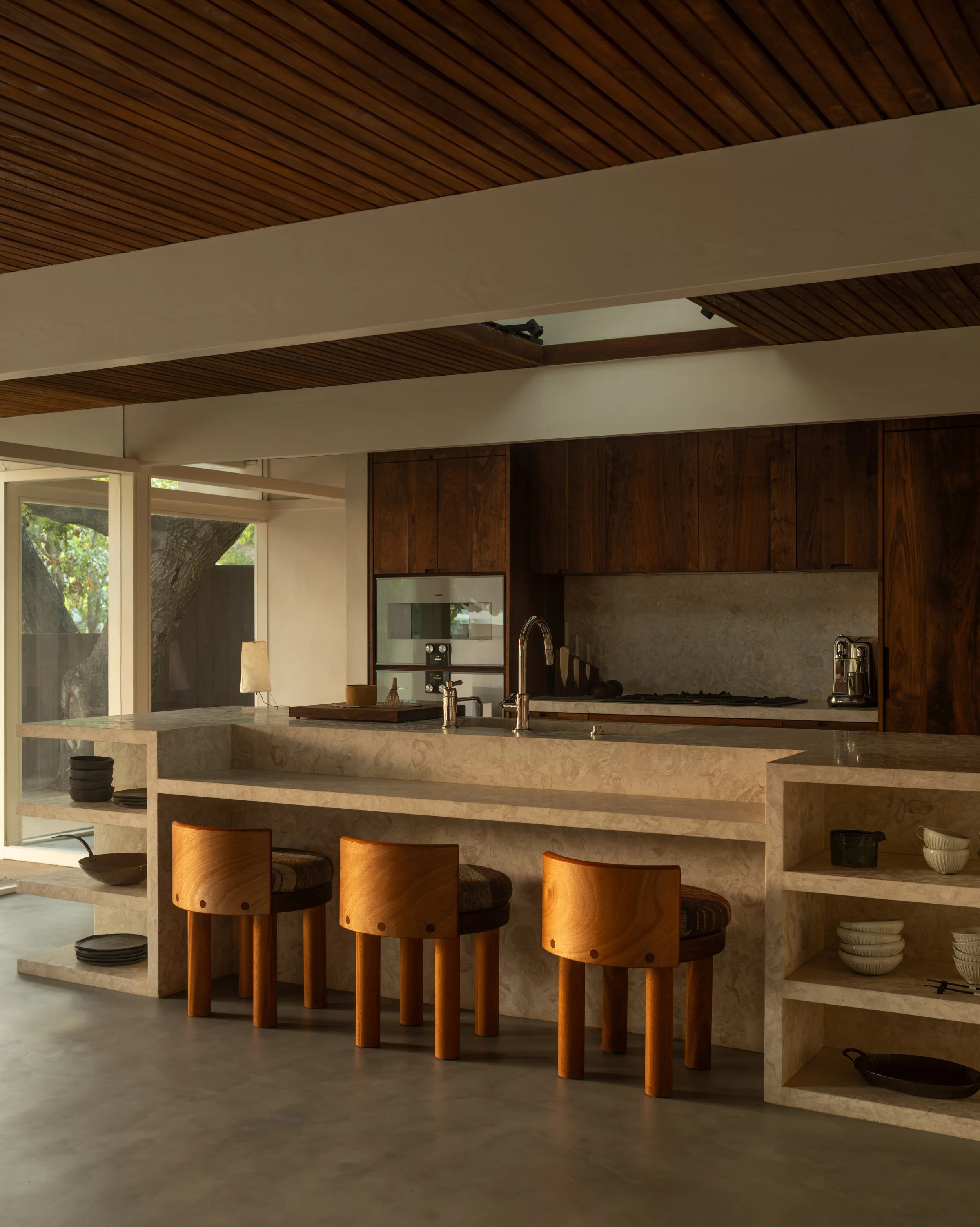 La Cuesta kitchen with custom walnut cabinetry, stone waterfall island, and built-in open shelving in warm natural light.