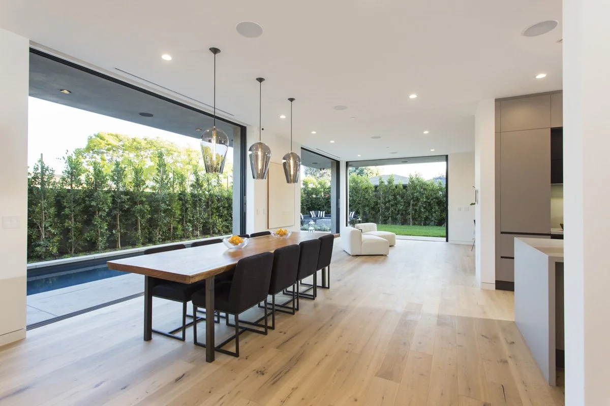 Venice open-concept dining area with floor-to-ceiling sliding glass walls, wide-plank oak flooring, and linear lap pool connection