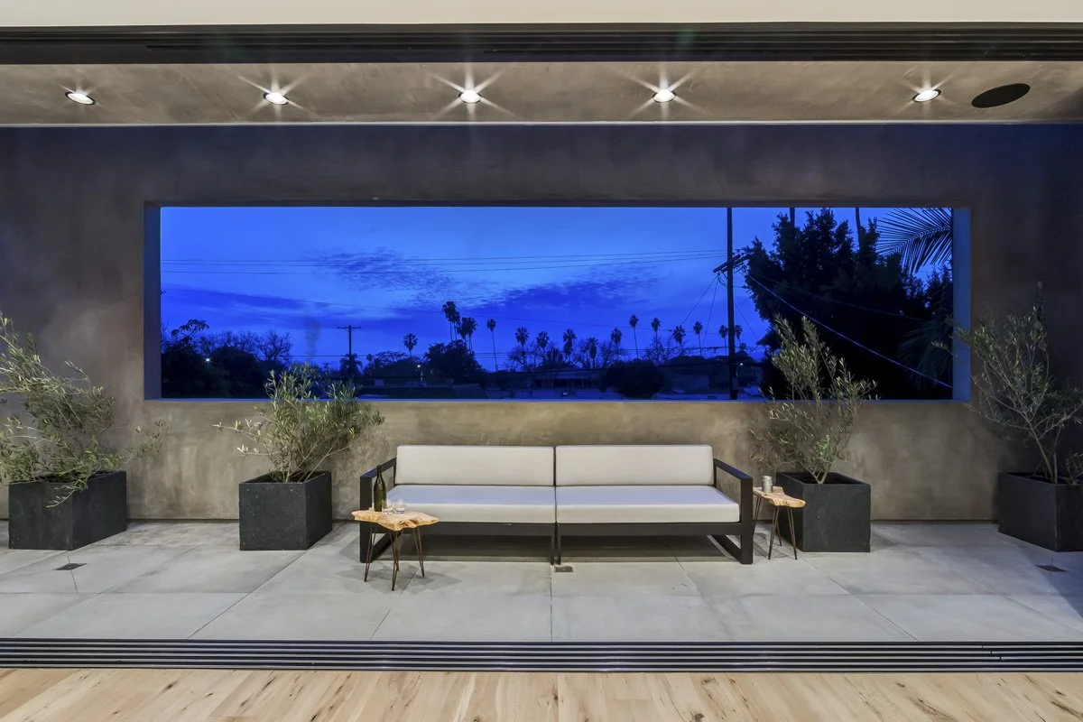 Modern West Hollywood terrace at dusk with framed panoramic window and built-in outdoor seating