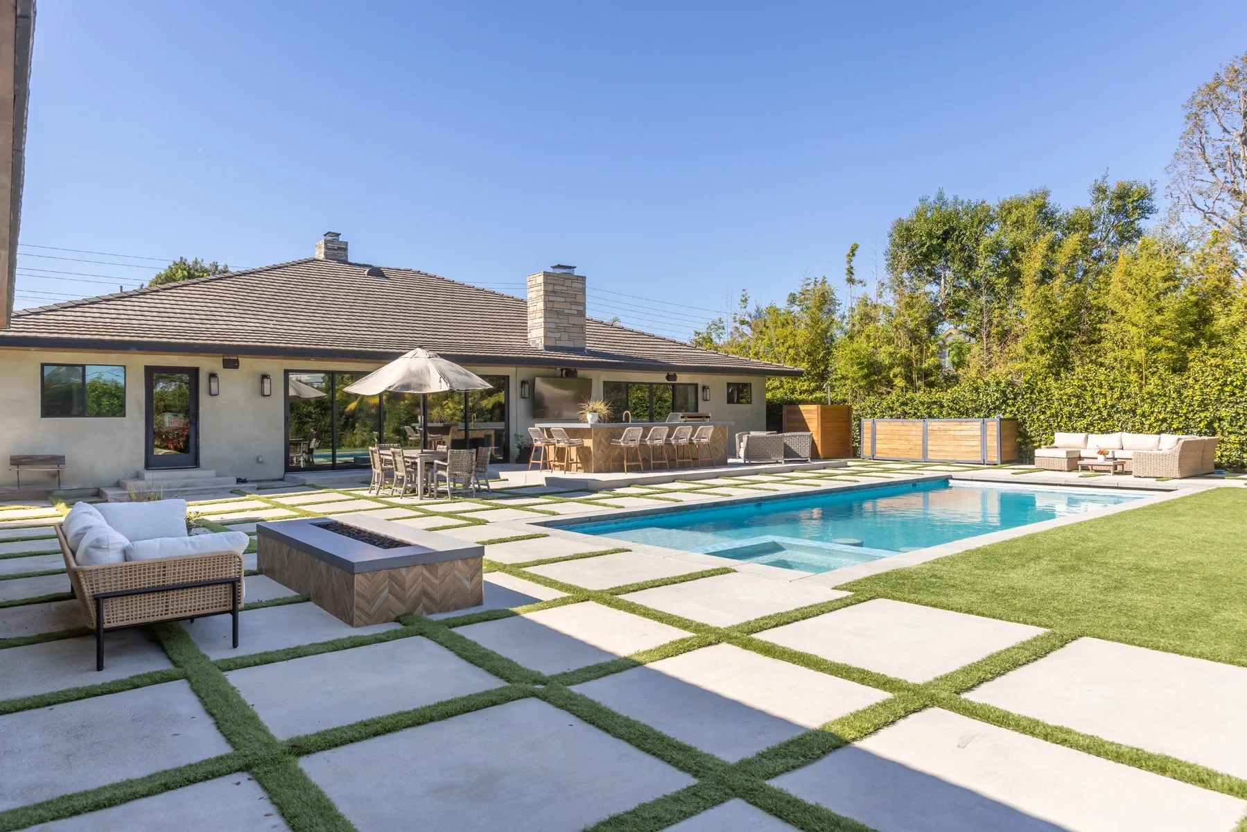 Outdoor living design and construction in Los Angeles featuring a custom pool, outdoor kitchen, fire pit seating, and modern hardscape by Heart Construction