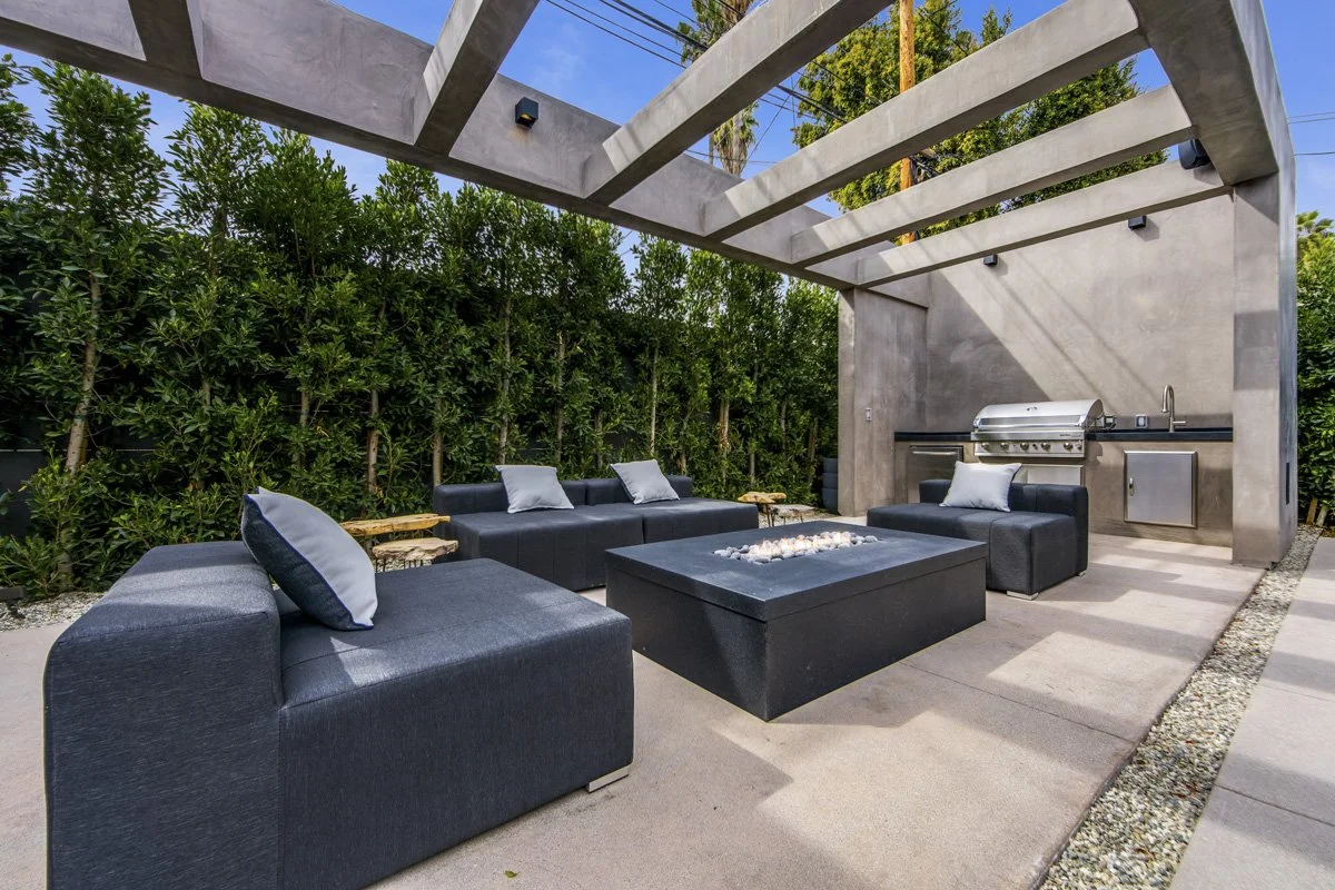 Brentwood outdoor living area with concrete pergola, built-in BBQ, fire feature, and private hedge-lined lounge space by Heart Construction
