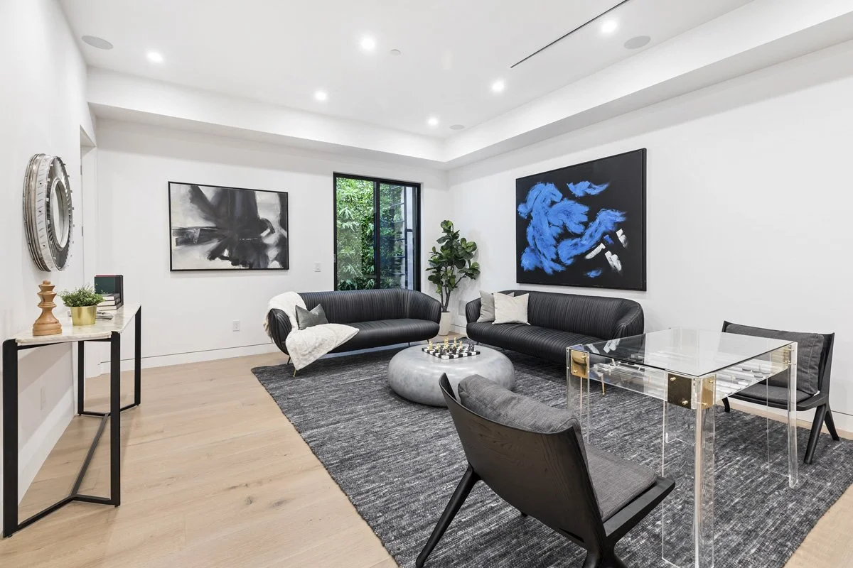 Beverly Hills lower-level lounge with curved black sofas, abstract blue artwork, and modern acrylic desk