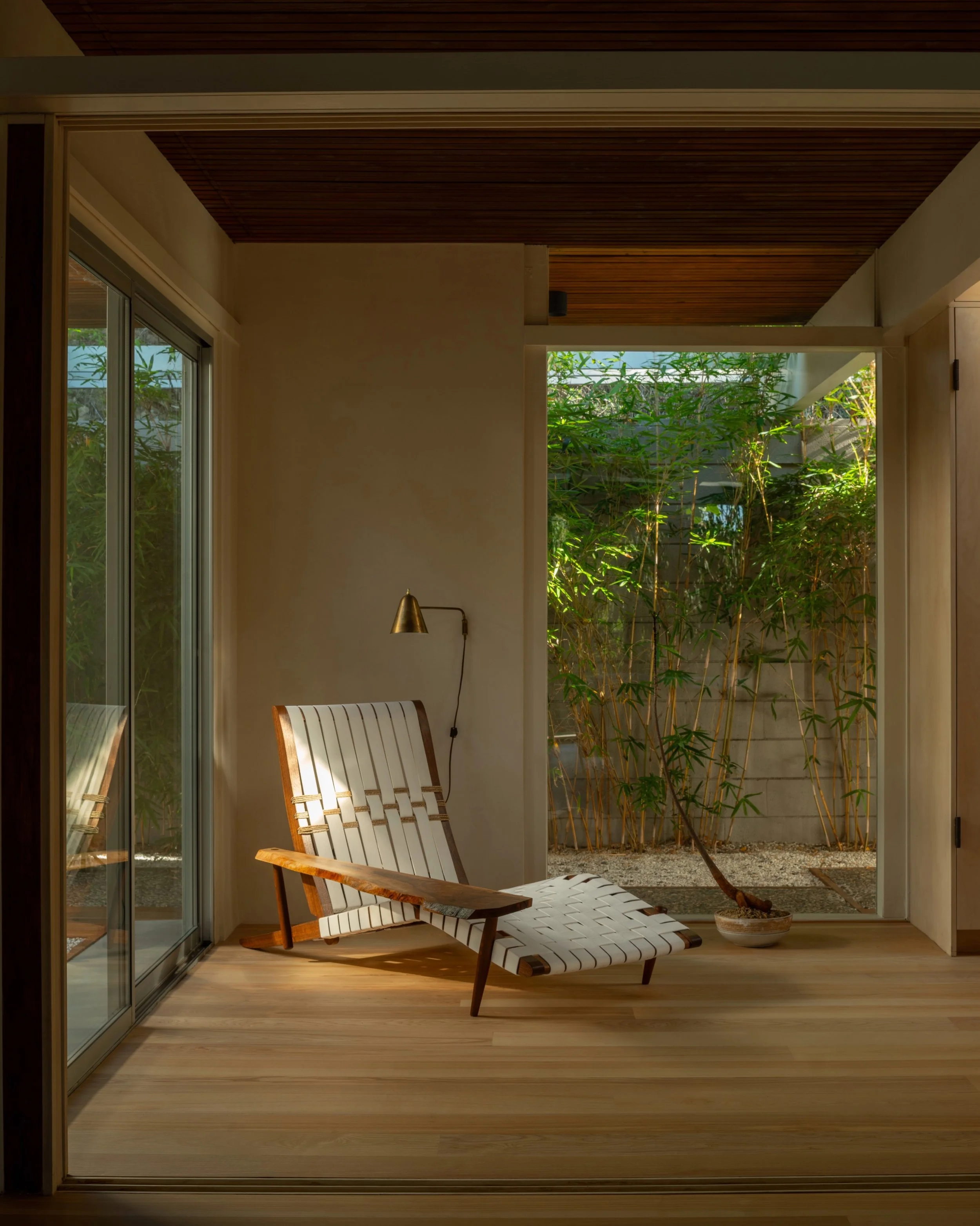 La Cuesta indoor-outdoor lounge with woven leather chaise, walnut ceiling, and floor-to-ceiling sliding glass doors opening to bamboo courtyard.