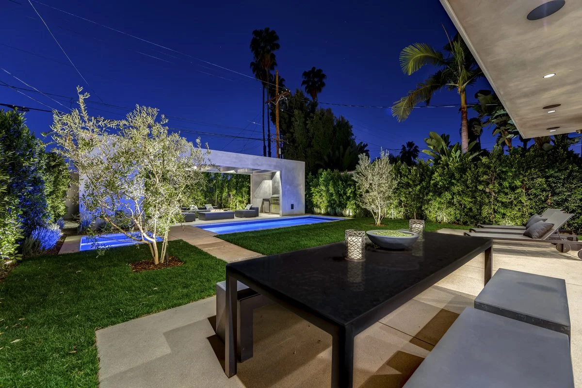 West Hollywood custom home backyard with modern pool, outdoor dining table, and illuminated pavilion at night