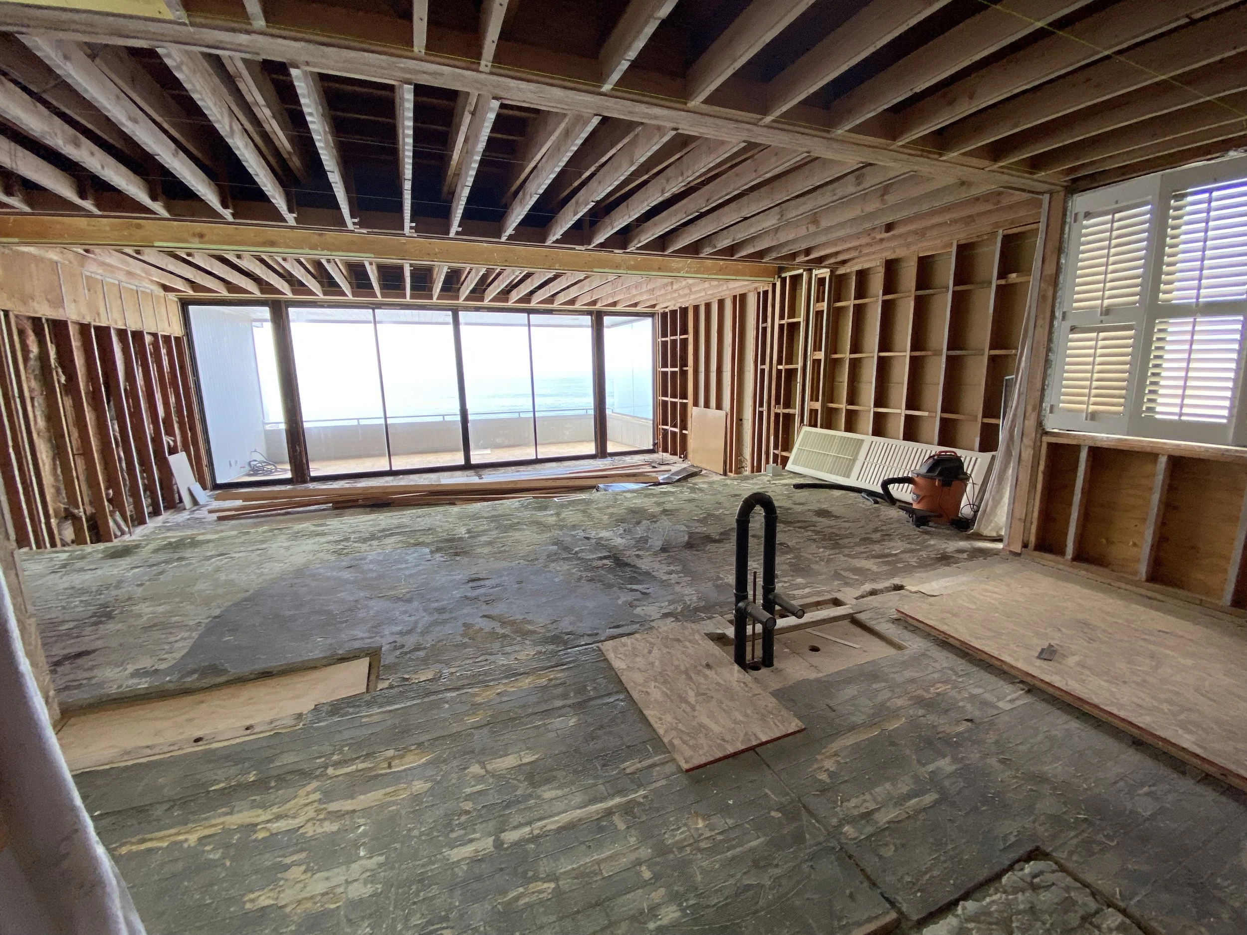 Malibu condo gut renovation in progress showing exposed framing and open structure aligned with ocean view through large sliding glass doors