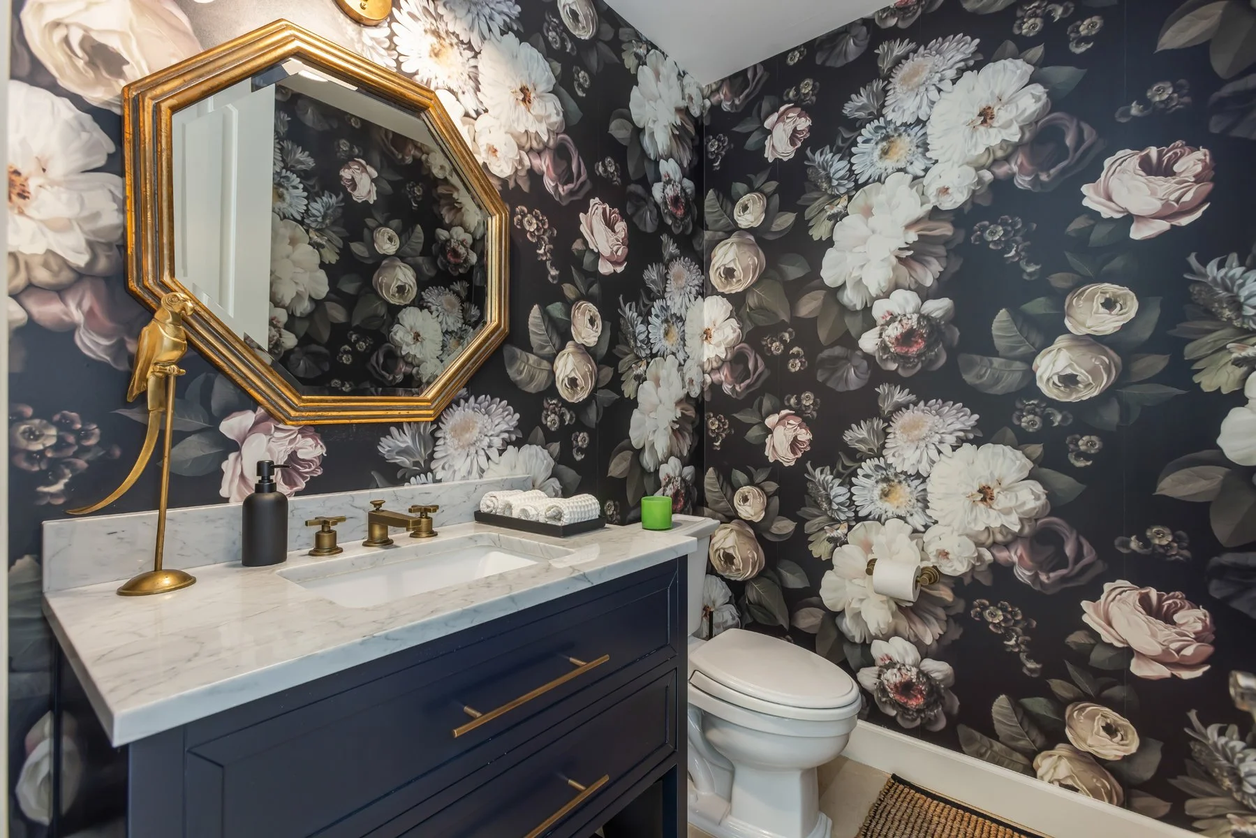 Powder bathroom in a custom Brentwood home featuring dramatic floral wallpaper, navy vanity with marble countertop, brass fixtures, and an octagonal mirror.