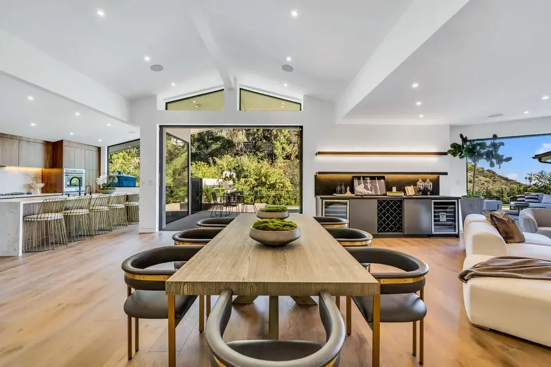 Modern open-concept living and dining area with large sliding glass doors leading to outdoor space, wooden flooring, minimalist decor, and natural light.