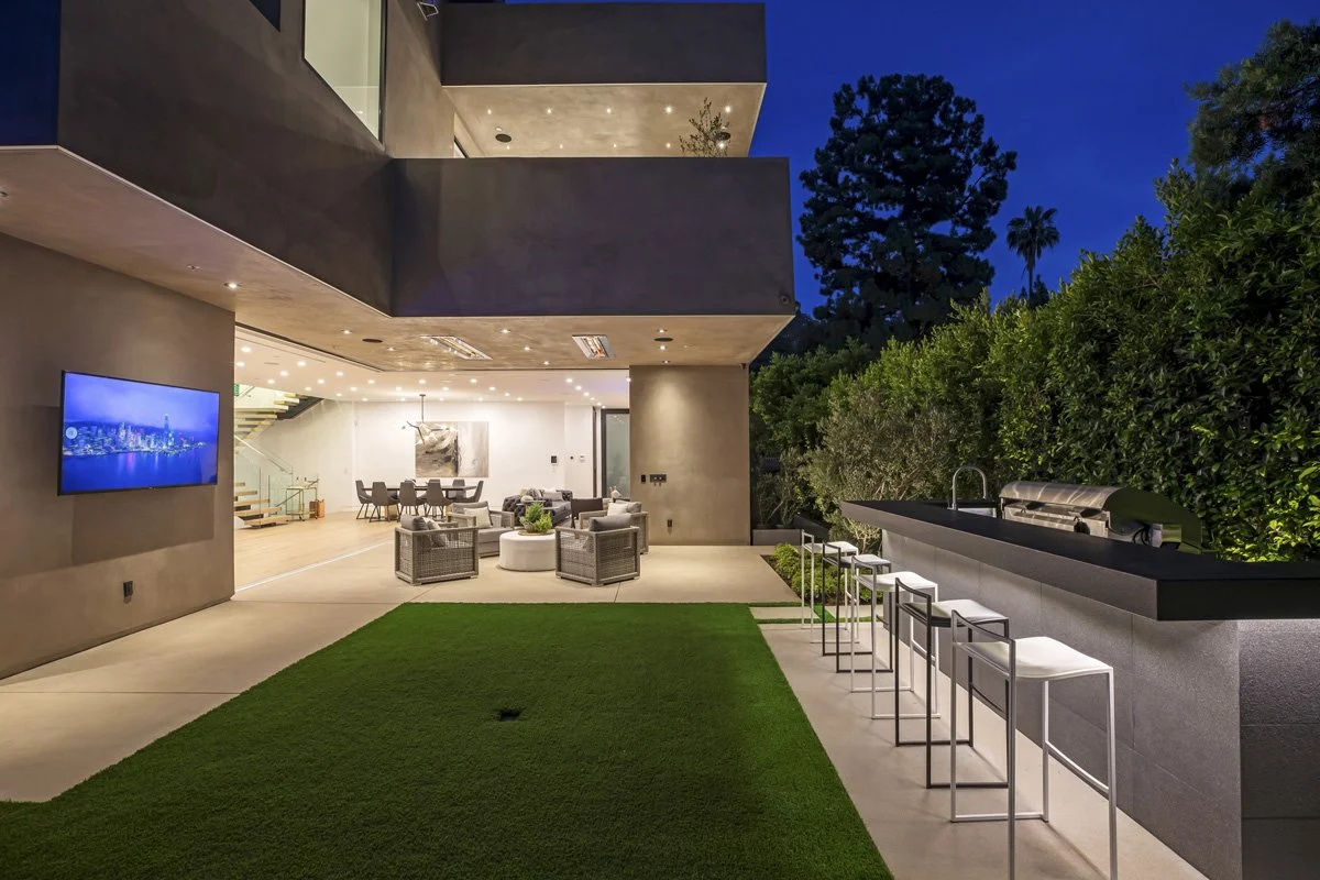 Culver City contemporary home with seamless indoor-outdoor living, covered patio lounge, outdoor kitchen bar seating, and open-plan interior illuminated at dusk.