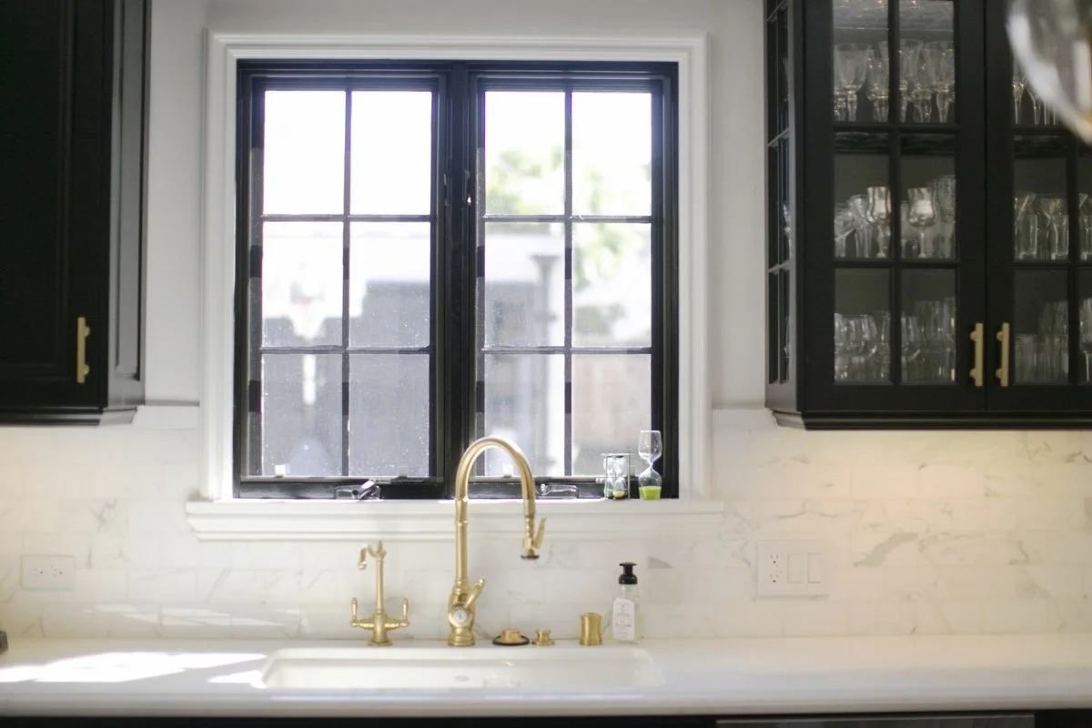 Kitchen sink detail with brass faucet, marble backsplash, and divided-light window in Hancock Park remodel