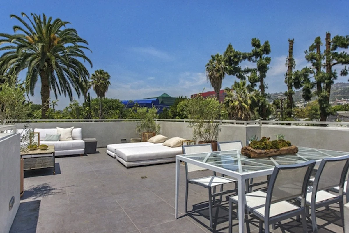 Rooftop terrace dining area in West Hollywood custom home with palm trees and city skyline views.